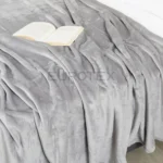 Coperta Plaid Dehor colore tortora distesa sul letto con libro aperto